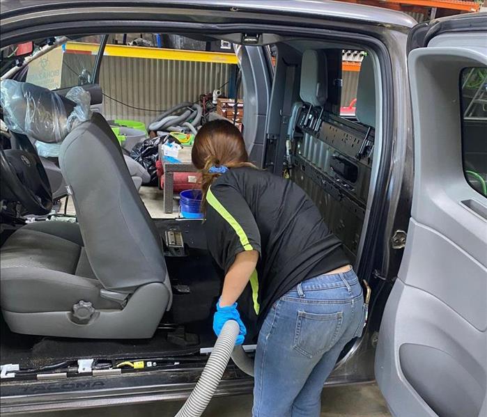 SERVPRO technician cleaning the interior of the extended cab of a silver pickup truck